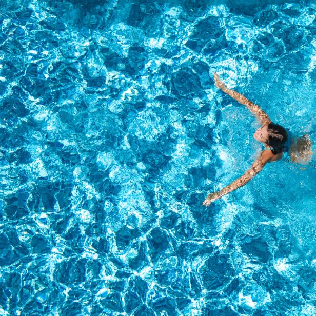 Aerial drone view of active girl in swimming pool from above, yong woman swims in blue water, tropical vacation, holiday on resort concept