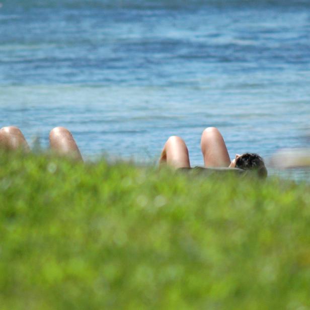Eine Person liegt im Gras mit Blick auf das Meer.