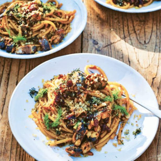 Drei Teller Pasta mit Pilzen und Kräutern auf einem Holztisch.