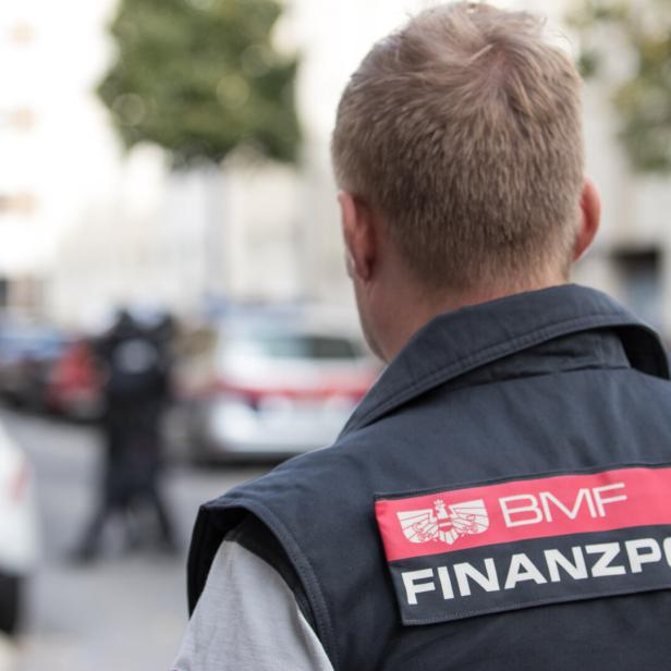 Ein Finanzpolizist steht auf der Straße, erkennbar an der Aufschrift „BMF Finanzpolizei“ auf seiner Jacke.