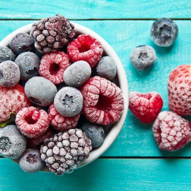 Gefrorene Himbeeren, Blaubeeren, Brombeeren und Erdbeeren in einer Schüssel auf einem türkisfarbenen Holztisch.