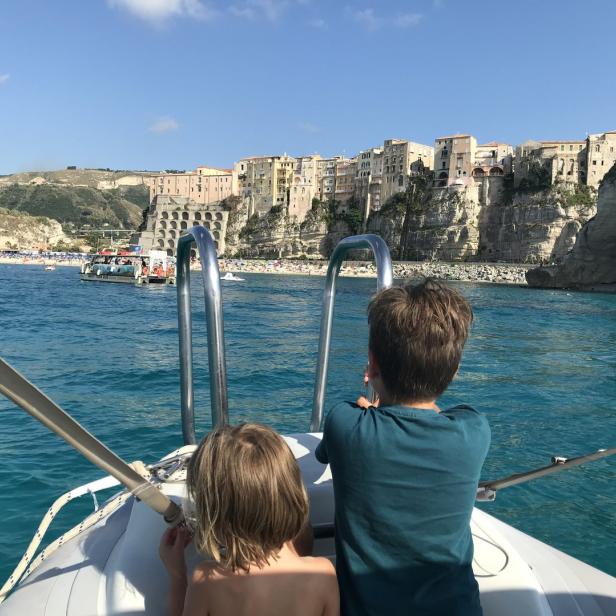 Zwei Kinder sitzen in einem Boot mit Blick auf die Küstenstadt Tropea in Kalabrien.