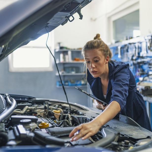 Lovely female auto mechanic, examining engine of an automobile