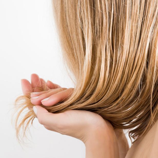 Eine Frau hält ihr langes, blondes Haar in den Händen.