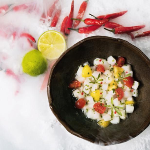 Ein Teller Ceviche mit Limetten und roten Chilischoten auf einem Tisch mit Trockeneis.