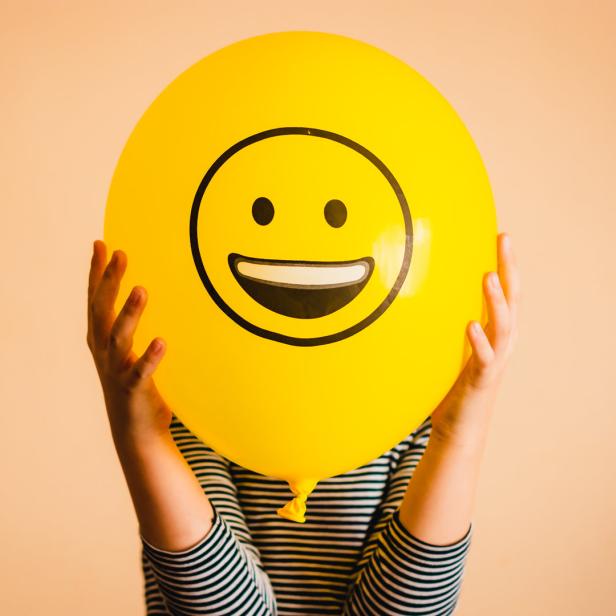 Ein Kind hält einen gelben Ballon mit einem Smiley-Gesicht vor sein Gesicht.