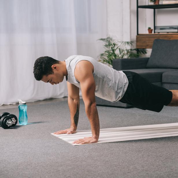 Ein Mann macht Liegestütze auf einer Yogamatte in seinem Wohnzimmer.
