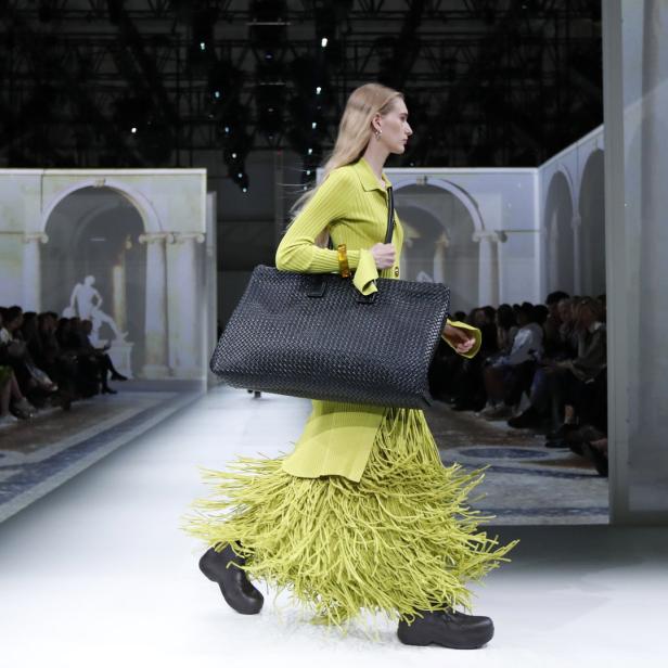 Ein Model läuft mit einer übergroßen, gewebten Tasche auf dem Laufsteg.
