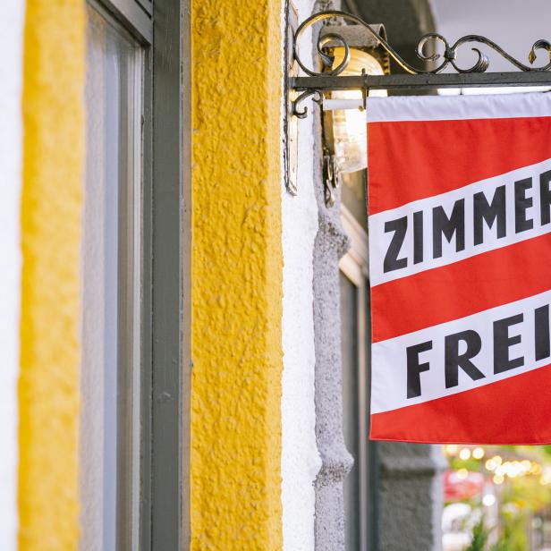 Ein Schild mit der Aufschrift „Zimmer Frei“ hängt an einer Hauswand.