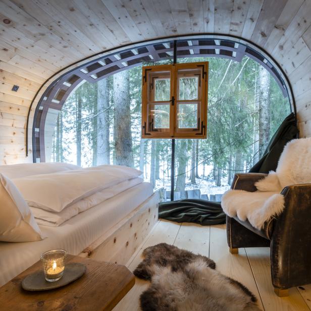 Ein gemütliches Zimmer mit Bett und Sessel bietet einen Blick auf einen verschneiten Wald.