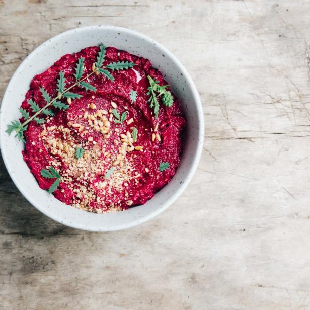 Eine Schüssel mit Rote-Bete-Hummus, garniert mit Nüssen und grünen Zweigen.