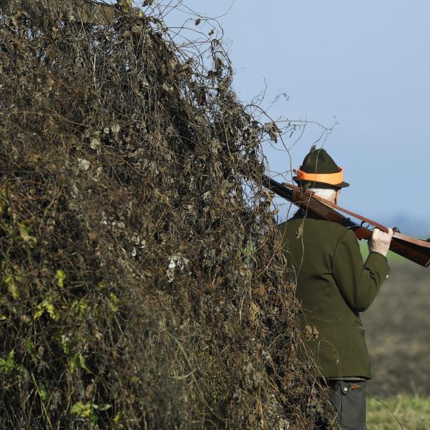 Ein Jäger mit Gewehr steht hinter einem Busch.