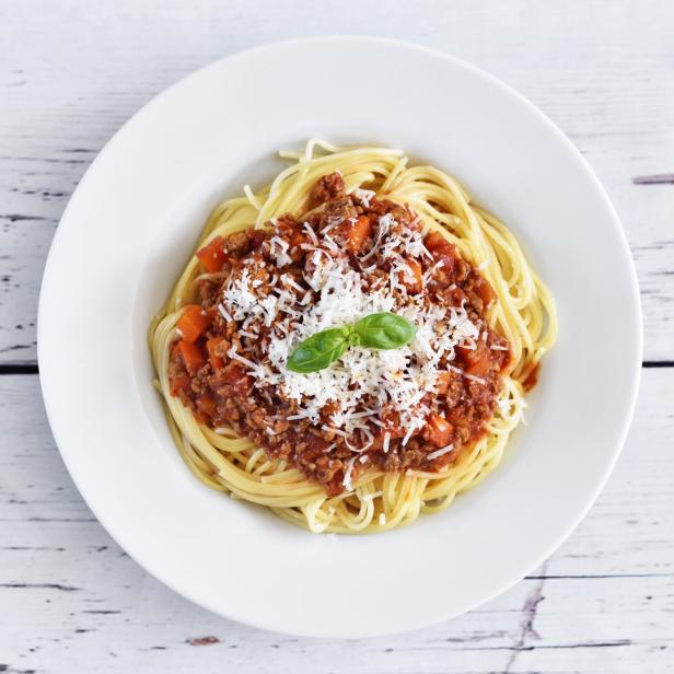 Ein Teller Spaghetti Bolognese, garniert mit Parmesan und Basilikum, auf einem Holztisch.