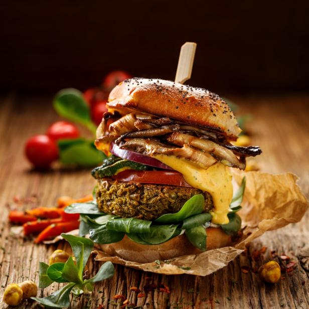 Vegan burger, green peas burger, homemade burger with green peas cutlet, grilled mushrooms, tomato, red onion, lamb's lettuce, and curry sauce on a wooden background.