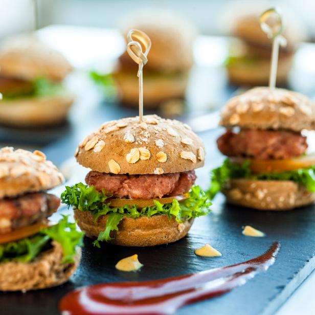 Mehrere Mini-Burger mit Salat und Tomaten auf einem schwarzen Teller.