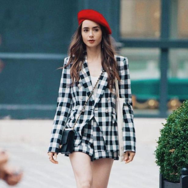 Lily Collins in einem schwarz-weiß karierten Hosenanzug und roter Baskenmütze.