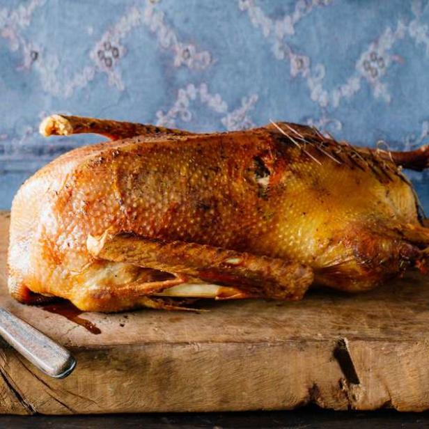 Ein gebratener Gänsebraten liegt auf einem Holzbrett.