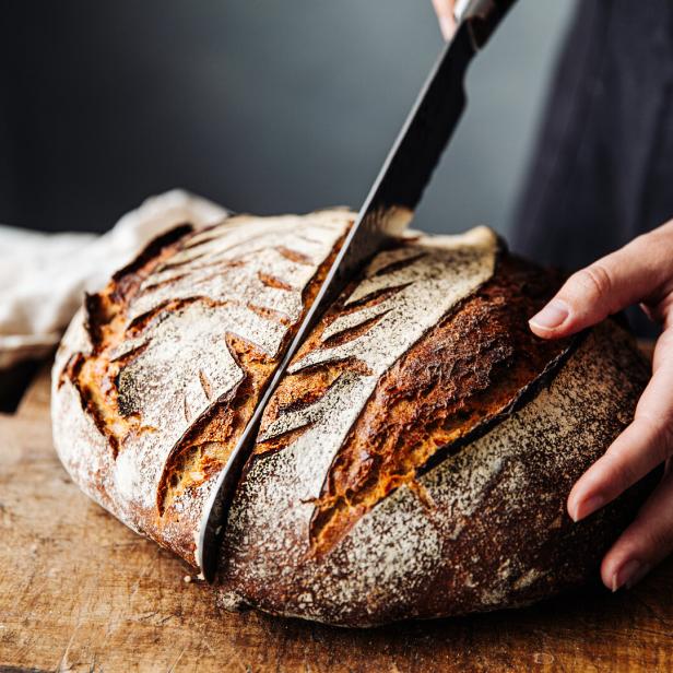 Ein Laib Brot wird auf einem Holzbrett angeschnitten.