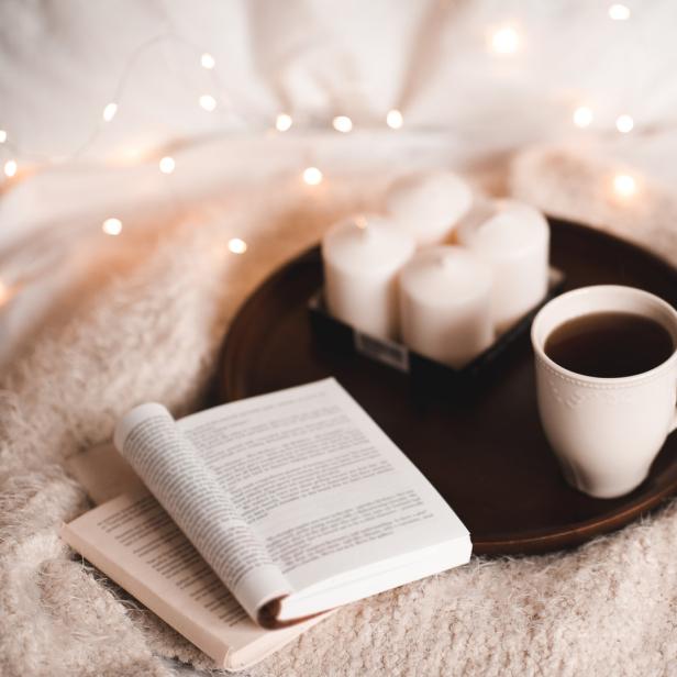 Eine Tasse Tee, ein Buch und Kerzen auf einem Tablett im Bett.