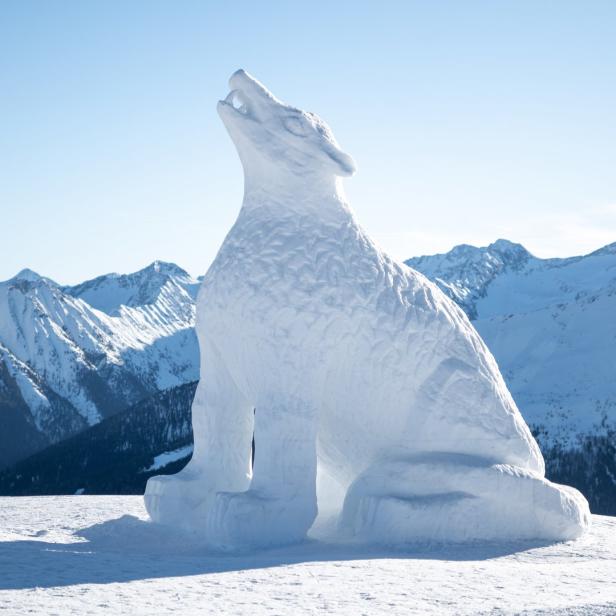 Eine Skulptur eines heulenden Wolfs aus Schnee vor einer Bergkulisse.
