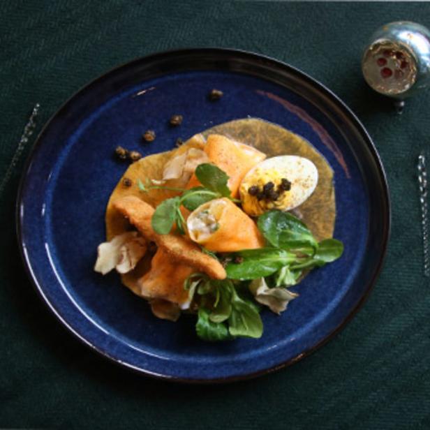 Ein Teller mit Lachs, Ei, Salat und Dekoration auf einem dunkelgrünen Tuch.
