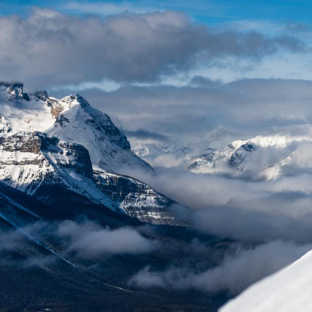 Ein Skifahrer in roter Jacke fährt einen schneebedeckten Hang hinunter, im Hintergrund Berglandschaft.