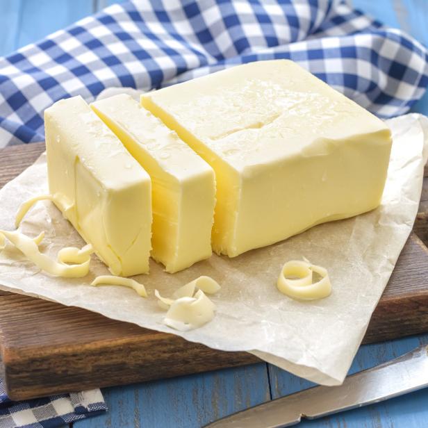 Ein Stück Butter, teilweise in Scheiben geschnitten, auf einem Holzbrett.