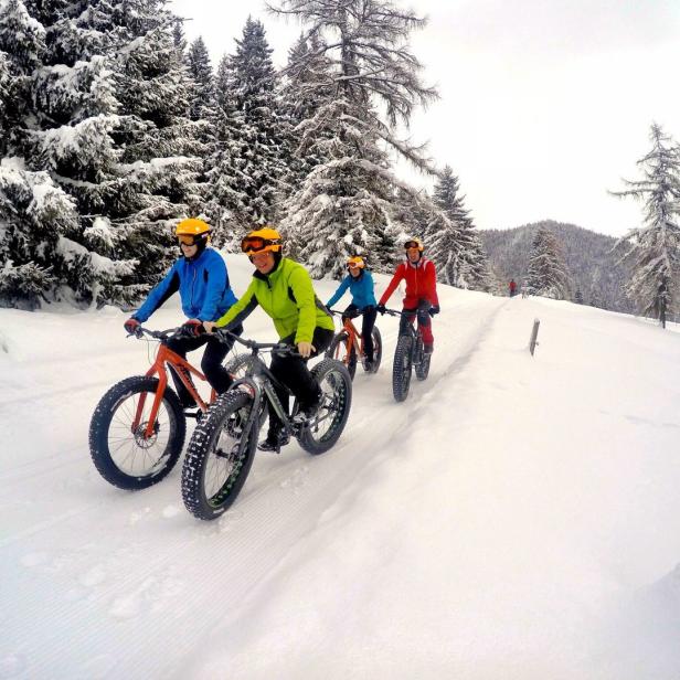 Eine Gruppe von Personen fährt mit Fatbikes auf einer schneebedeckten Piste entlang.