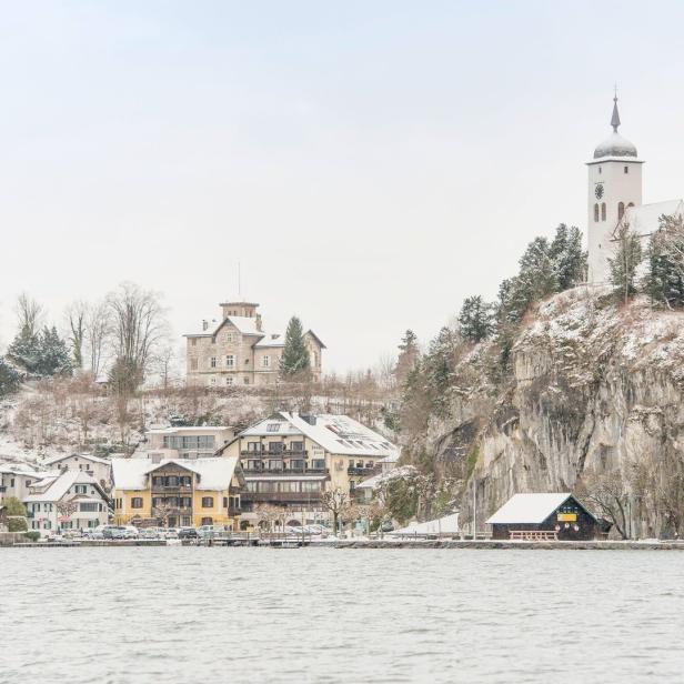 Blick auf ein Dorf am See mit einer Kirche auf einem Hügel im Winter.