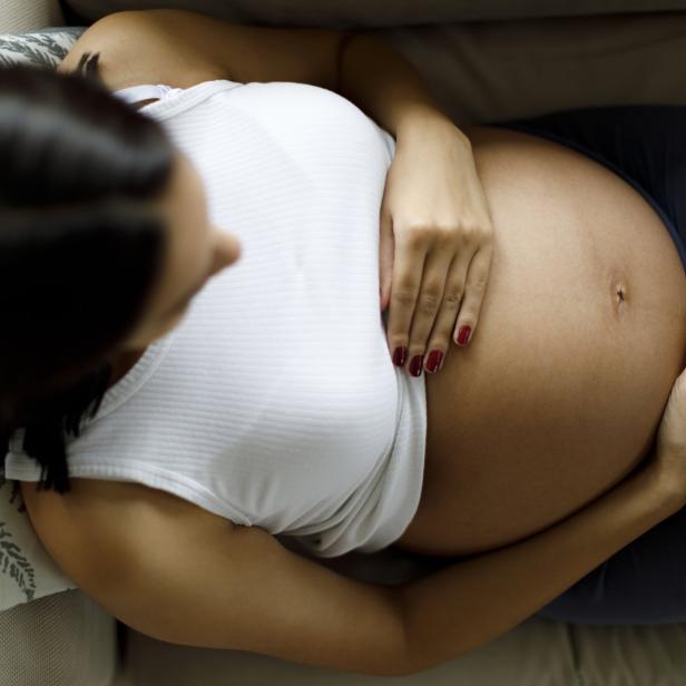 Eine schwangere Frau greift sich auf den Bauch.