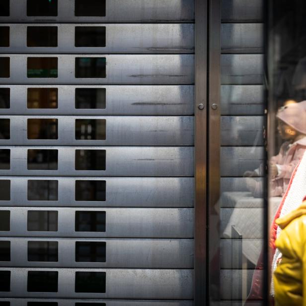 Zwei Schaufensterpuppen mit Winterkleidung stehen hinter einem teilweise geschlossenen Metallrolltor.