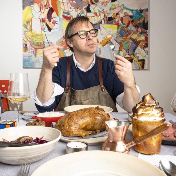 Ein Mann mit Brille isst an einem reich gedeckten Tisch mit Ente, Rotkohl und Dessert.