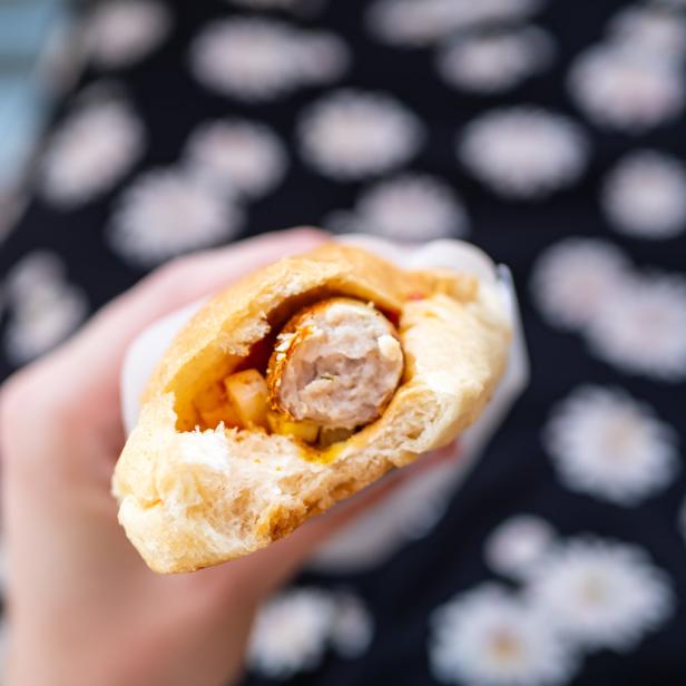 Eine Hand hält ein halbes Hotdog mit Wurst und Soße.
