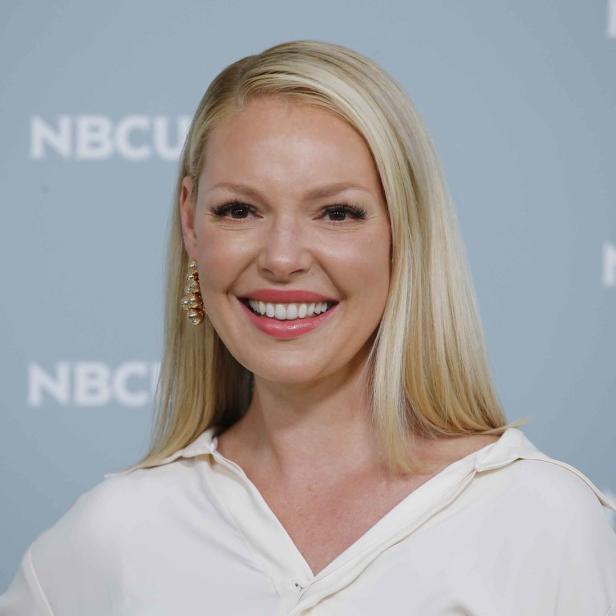 Katherine Heigl lächelt vor einem Hintergrund mit dem NBCU-Logo.