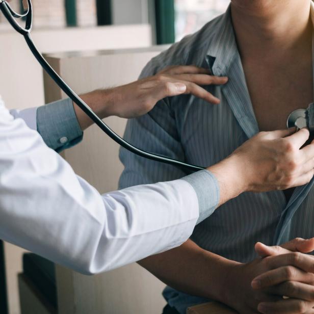 Arzt untersucht mit Stethoskop den Brustkorb eines sitzenden Patienten.