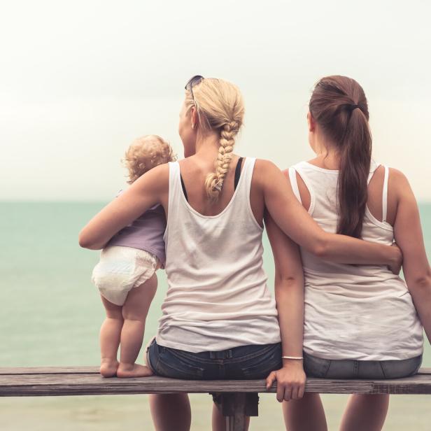 Zwei Frauen und ein Kleinkind sitzen auf einer Bank mit Blick auf das Meer.