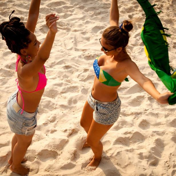 Zwei Frauen am Strand, eine mit einer brasilianischen Flagge.