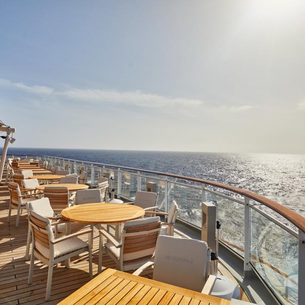 Ein Restaurantbereich mit Tischen und Stühlen auf dem Deck der MS Europa 2 mit Blick auf das Meer.
