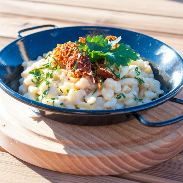 Eine Portion Käsespätzle mit Röstzwiebeln und Petersilie in einer schwarzen Pfanne.