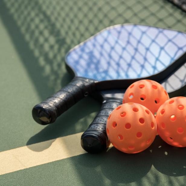 Zwei Pickleball-Schläger und drei orangefarbene Bälle auf einem Pickleball-Feld.