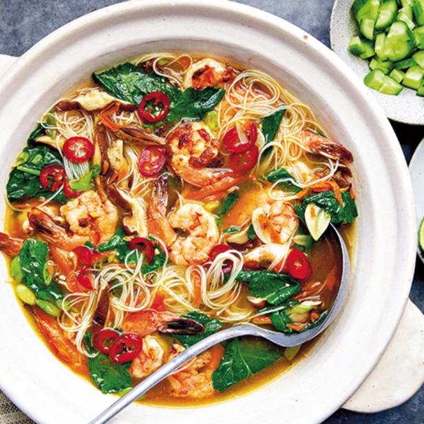 Eine Schüssel mit Garnelensuppe, Nudeln, Gemüse und Limetten auf einem Tisch.
