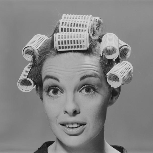 Eine Frau mit Lockenwicklern im Haar blickt in die Kamera.