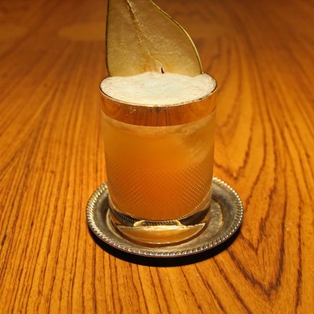 Ein Cocktail mit Birnenscheibe als Dekoration auf einem Holztisch.