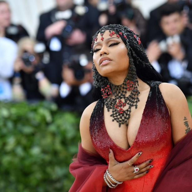 Nicki Minaj posiert in einem roten Kleid und auffälligem Schmuck auf dem roten Teppich.