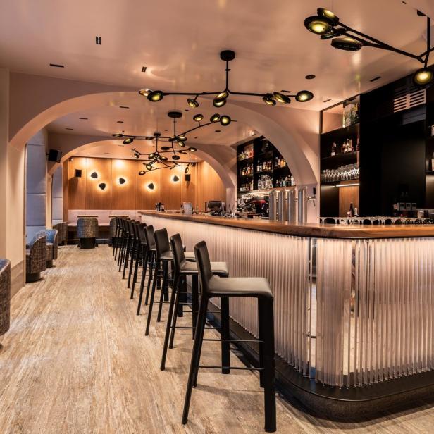 Eine Bar mit Hockern und einer beleuchteten Theke in einem eleganten Interieur.