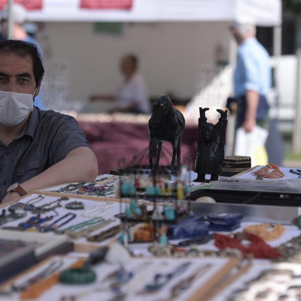 Ein Mann mit Maske sitzt an einem Stand mit Schmuck und kleinen Statuen.