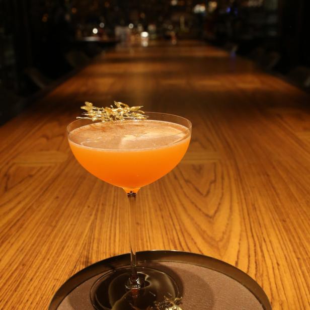 Ein Cocktail mit goldener Dekoration steht auf einem Holztisch.