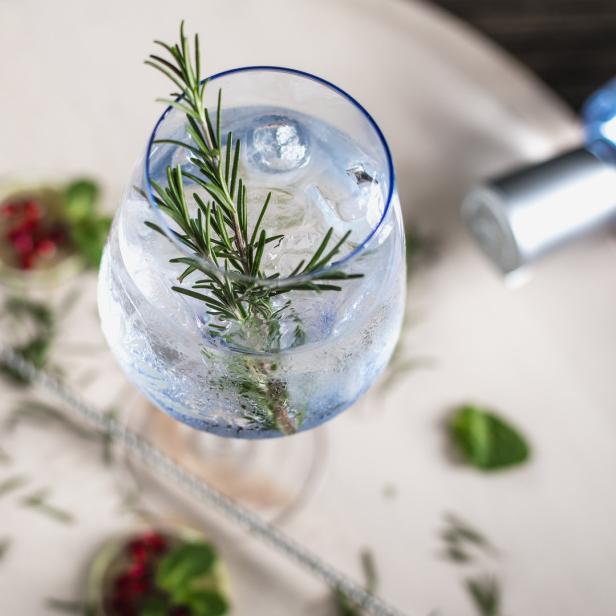 Ein Gin Tonic mit Rosmarin und Eiswürfeln auf einem Tablett.