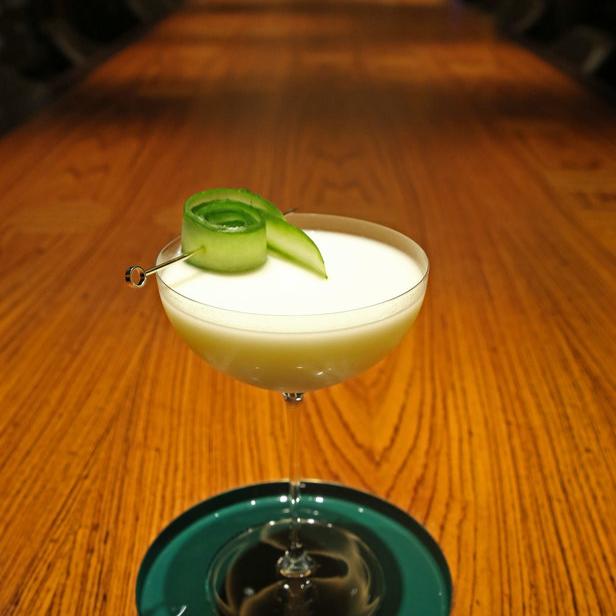 Ein Cocktail mit Gurkengarnitur steht auf einem Holztisch.
