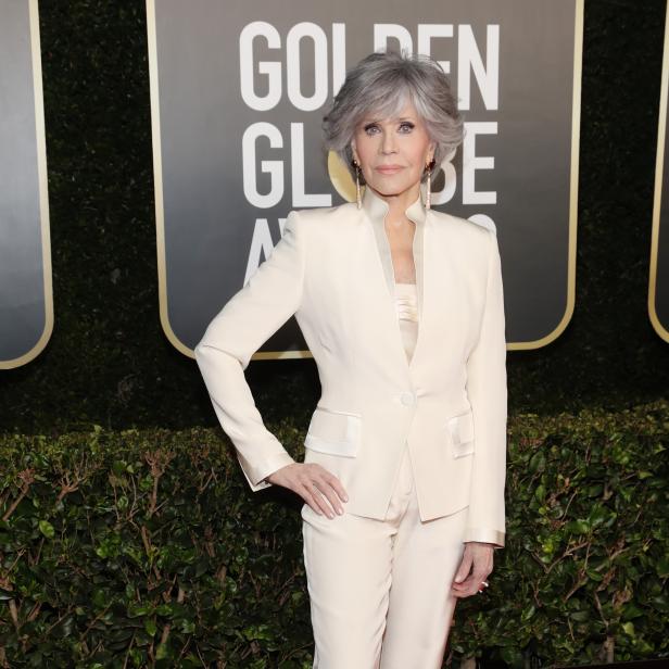 Jane Fonda in einem weißen Hosenanzug auf dem roten Teppich.